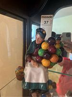 Frontal view of the Royal Doulton Balloon Seller figurine showing full figure, headscarf, balloon cluster, basket, and seated posture.