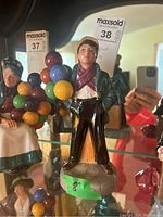 Porcelain figurine of a young man with colorful balloons, signed Michael Doulton, standing on a grey stone base with an 8 inch label.