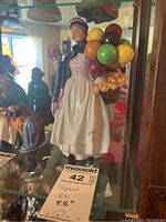 Front view showing the full figure of a woman in period dress with balloons and basket.