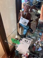 Front and side view of the Royal Doulton figurine showing man sitting on stump holding a telephone receiver and newspaper with a box of newspapers beside him.