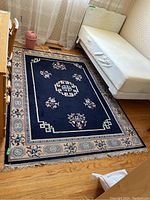 Full view of the navy blue area rug placed on wooden flooring next to a bed and furniture, showing overall condition and size.