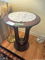 Round wood pedestal side table with dark finish and lace doily on top, visible stain on surface.