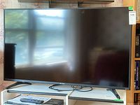 Front view of TV on stand with remote and manual visible on shelf below