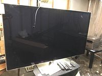 Head-on view of TV on stand with power cord and remote controls visible on table