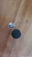 Matte black round cabinet knob next to a coin for size reference, showing knob diameter about 1 inch.