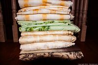 Stack of 8 folded duvet covers in different patterns and colors showing floral and abstract designs in warm muted tones.