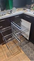 Kitchen corner cabinet with three pull-out wire baskets extended, attached door with chrome handle