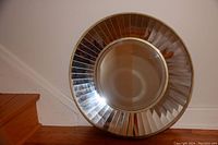 Round mirror leaning against a wall and stairs showcasing its faceted reflective glass frame and central circular mirror surface. The frame is divided into angular segments that reflect light. Image captures the full mirror and its size relative to the stairs.