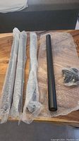 Four black metal table legs, wrapped in bubble wrap, laid out on wood surface.