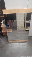 Full view of large rectangular mirror mounted in a light wood frame standing against a wall, showing its size and general condition.