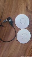 Pair of UniFi WiFi access points shown with PoE adapter, all placed on wooden surface.