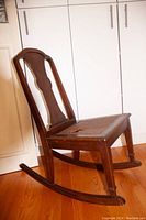 Side view of vintage wooden rocking chair showing curved rockers, shaped backrest panel, and cane seat with hole.