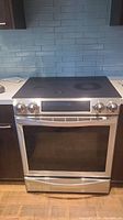 Frontal view of induction range installed in kitchen showing control knobs, oven door and warming drawer.