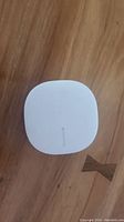 Front top view of the white Samsung SmartThings Hub placed on wooden surface.