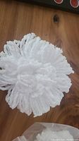 Close-up top view of white microfiber mop head strands arranged in a circular pattern on wooden surface.
