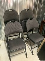 Four black metal folding chairs stacked with cushioned seats and backs, showing upholstery and frame details.