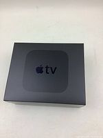 Closed Apple TV box showing matte black finish with Apple logo and 'tv' branding on top.