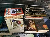 Photo showing a collection of art books and novels stacked on a shelf including '20th Century in Cartoons,' 'Rodin,' and 'The Goldfinch'.