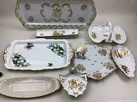 Overall display of eight assorted vintage fine china serving pieces featuring white and gold floral designs, scalloped edges, and a handled dish.