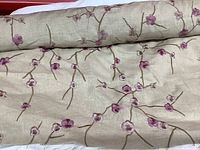 Close-up photo showing the embroidered purple cherry blossom flowers and brown branches on beige linen fabric, highlighting fabric texture and embroidery details.