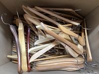 Box filled with a pile of wooden clothes hangers showing a variety of wood tones and styles.