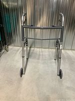 Front view of the folding walker showing metal tubing frame, front wheels and rubber grips on handles.
