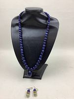 Full view of blue lapis natural stone bead necklace displayed on black jewelry bust with matching earrings in front.