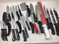 Photo of all knives and utensils laid out showing blades and handles, various sizes and styles of kitchen knives including cleaver and sharpeners.