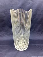 Front angled photo showing the large clear glass vase with vertical ribbed lines and wavy top rim, standing on a dark blue surface.
