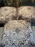 Photo showing the set of three square throw cushions with a symmetrical neutral medallion pattern on fabric, arranged with one cushion in front and two in back.