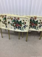 Three vintage TV trays leaning against a wall, showing the matching floral and butterfly print on cream backgrounds.