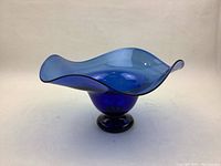 Blue signed art glass bowl photographed from a side angle showing the flowing, wavy rim and pedestal base.