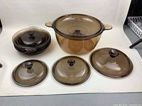 Grouped image showing large Vision casserole with lid, three smaller amber lids, and stacked four small Pyrex bowls with lids.