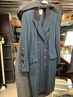 Full front view of the blue vintage striped jacket with gold buttons and black satin collar, hanging in front of the garment bag.