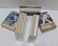 Five stacks of assorted baseball cards arranged on white surface, some wrapped in plastic and some loose with visible player images