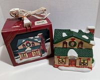 Front and box of Christmas Village lighted general store ceramic house with electric cord and plug coiled on top of box.