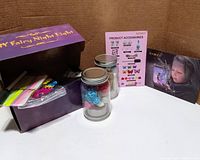 Box with purple labeling 'Fairy Night Light' showing contents including decorated glass jars, glow sticks, LED tealight candles, decorative accessories, and instruction pamphlet.