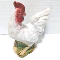 Front view of the ceramic rooster figurine showing white body, red comb, and green base.