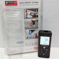 Front view of Leica DISTO E7400x with screen displaying measurements and info card in background showing product features.