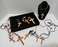 Photo of wooden crosses laid out on black tray and displayed on mannequin bust, various strings and cords visible.