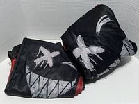 Photo of folded black hoodie with large white graphic, including 'X' shapes and a teeth-like pattern.