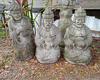 Front view of three concrete Three Wise Men statues showing detailed faces, headdresses, and gifts they hold. They are set outdoors on ground covered with leaves.