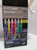 Box of Lightshow LED Synchro Lights showing brand, product name, and features including multicolor mode, 12-icicle set, 11 ft length.