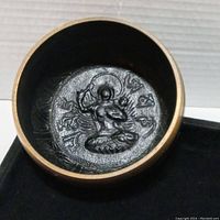 Close-up of interior of the beggars bowl showing embossed seated figure with surrounding script.