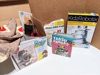 Photo of four items: Trash Pandas card game, Pee Jay sock monkey kit in box, KidzRobotix tin can robot kit box, and Picket Fence plant set with wood blocks and flower pots.