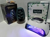 Display of UV gel nail lamp illuminated with purple light, ceramic incense burner and boxes visible