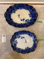 Top view of two oval flow blue platters with visible decorative floral pattern and scalloped borders; green stickers noting dimensions on platters; masold tag with lot number.