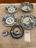 Overview of all six china pieces including four larger bowls/dishes, teacup, saucer, and dresser jar with lid placed on a light rug background.