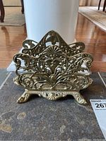 Front view of ornate vintage brass letter holder showing detailed filigree and floral scroll design, on decorative feet.