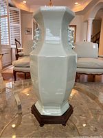 Full view of the pale green celadon-style hexagonal vase on a carved wooden stand placed on a glass table in a room